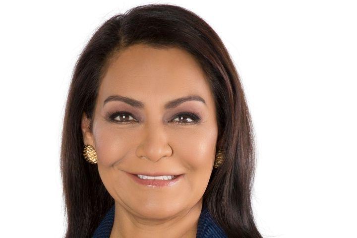 Headshot of woman with blue blazer, dark hair and gold earrings