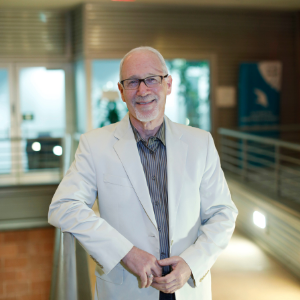 Man with white hair wearing black rimmed glasses and white jacket